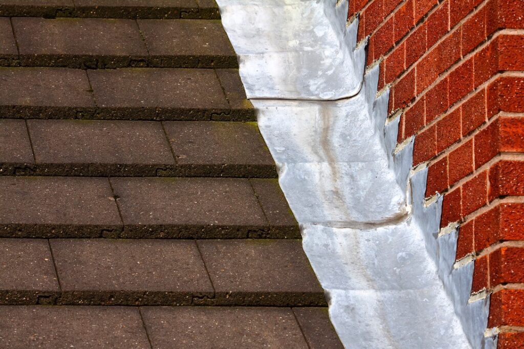 Stepped lead flashing roof gulley creating a water tight seal between roof tiles and brick wall on a domestic house