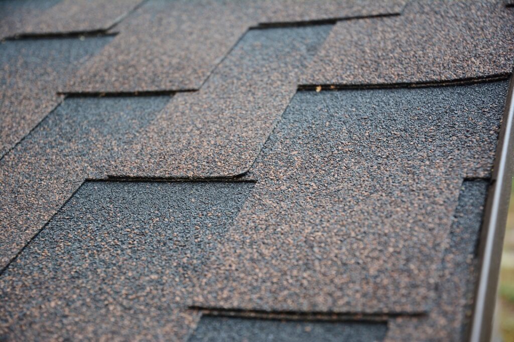 A close-up on architectural asphalt shingles installed on a roof.  Brown dimensional asphalt shingles roofing background.