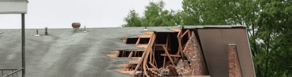 A multi-family property roof with severe damage caused by high winds and debris.