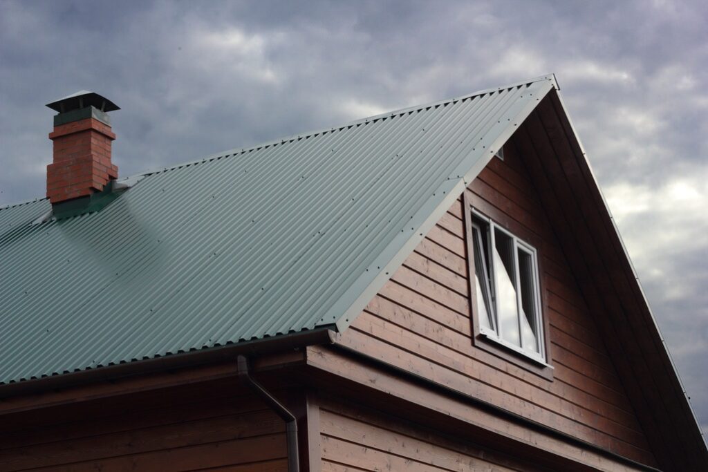 Green metal roof and brick chimney under cloudy sky photo