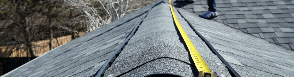 A close up image of a roofing contractor with his tape measure, measuring the slope of a residential roof. Measuring is a crucial step before installing impact-resistant shingles.