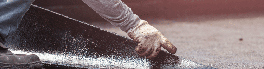A close up image of a roofer laying down a rubber roofing layer.